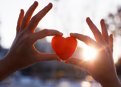 Hands holding up a toy heart in the sunshine